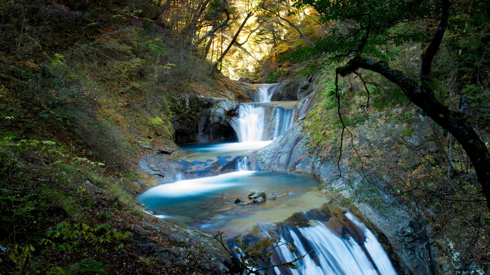 Enchanting autumn scene of Nishizawa Valley with waterfalls, foliage, and serene atmosphere in Japan.