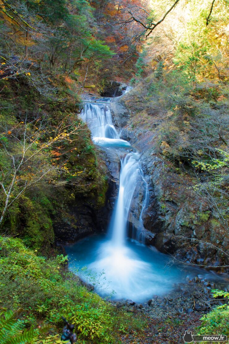 Enchanting autumn waterfall cascading through lush forest with vibrant trees in stunning hues.