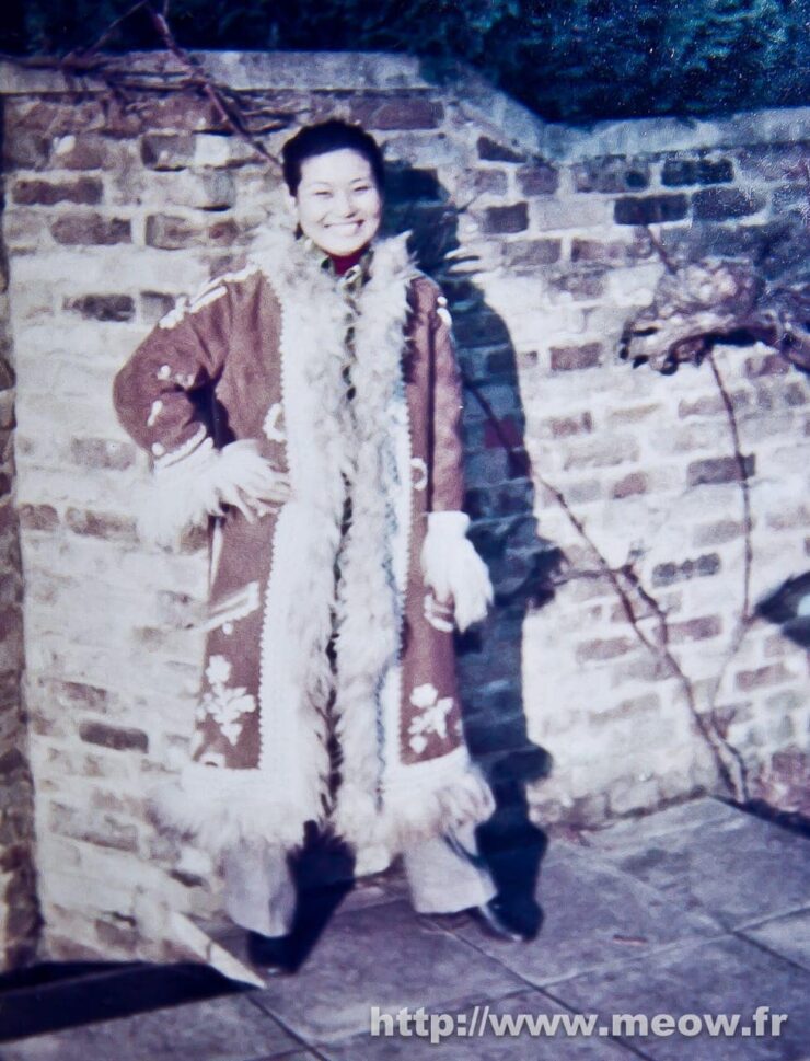 Stylish woman in light fur coat posing in front of brick wall outdoors.