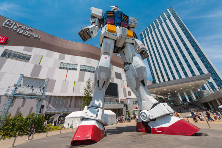 Impressive RX-78-2 Gundam statue in urban setting with bustling crowd and modern buildings.