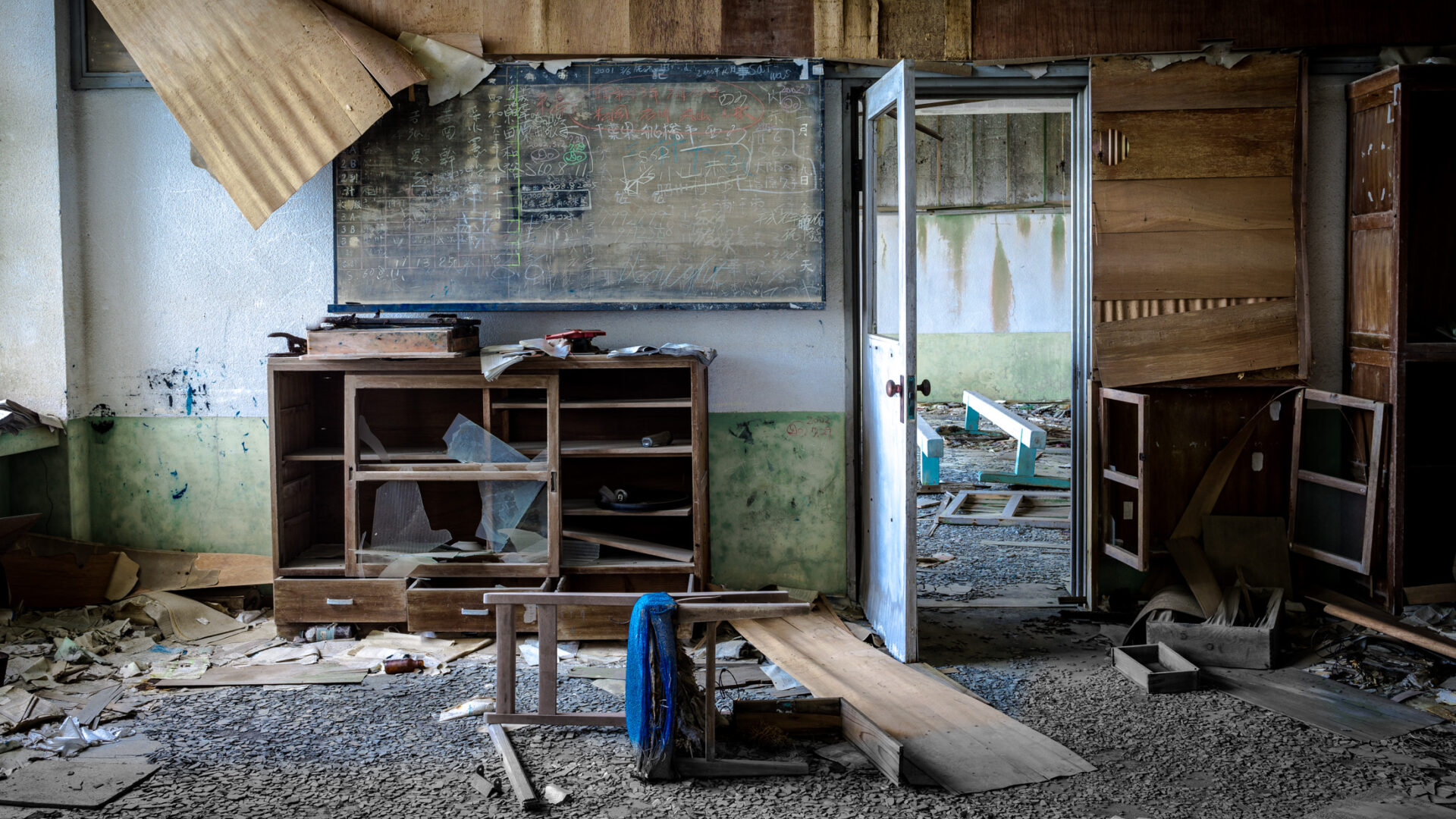 Abandoned teacher’s room on Gunkanjima, Japan, with faded chalkboard and debris-covered floor.