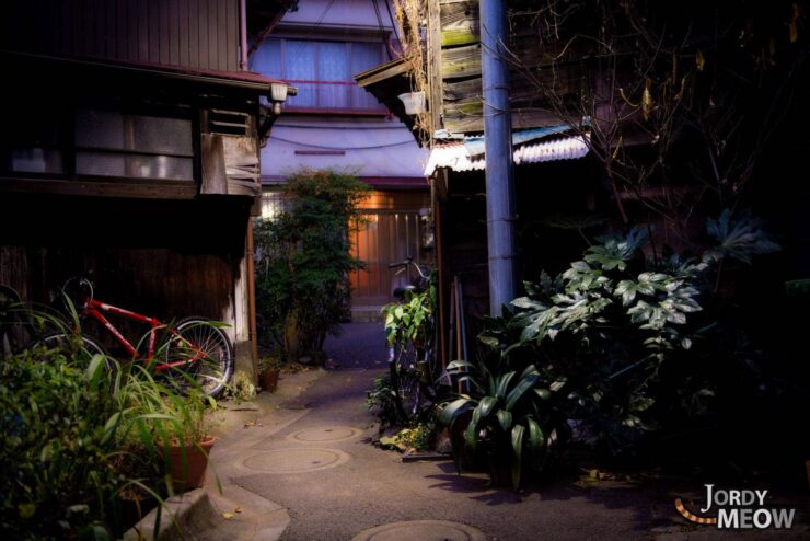 Tranquil Japanese alleyway at night with historic architecture, lush greenery, and a red bicycle.