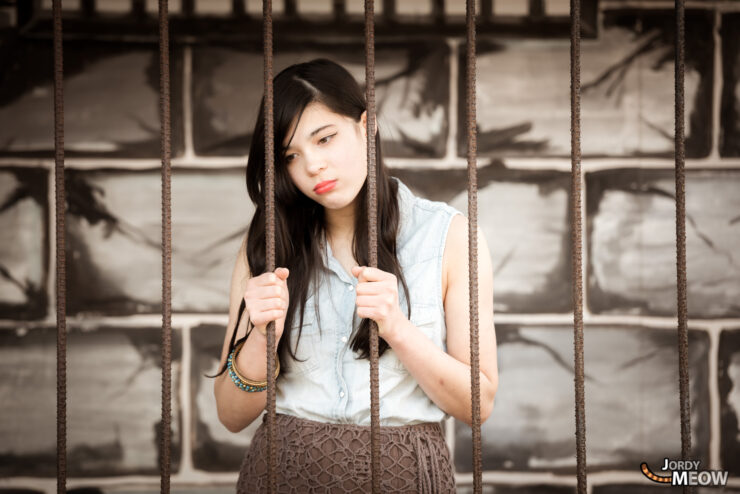Young woman in abandoned Western Village theme park, Japan, behind metal fence.