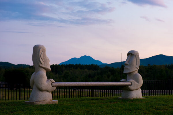 Enigmatic Moai statues in Hokkaido wilderness, framed by mountains and bathed in golden light.