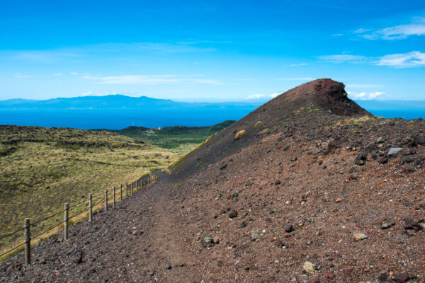 Explore Oshima Islands volcanic beauty with winding path, crater views, and ocean backdrop.