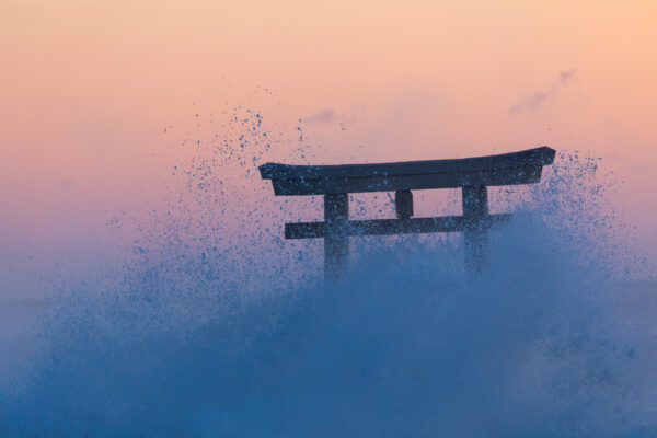 Sunset view of majestic Oarai Isosaki Shrine with torii gate and crashing waves.