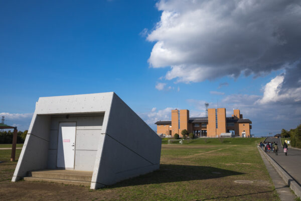 Concrete drainage structure in grass field efficiently manages water flow amid buildings under clear blue sky.