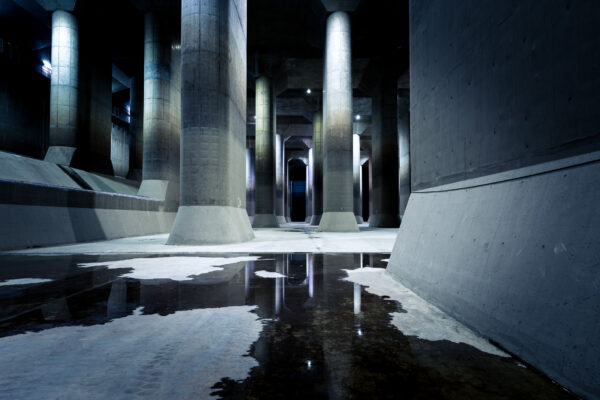 Subterranean water channel with massive pillars, arched ceilings, and spotlit water reflections.