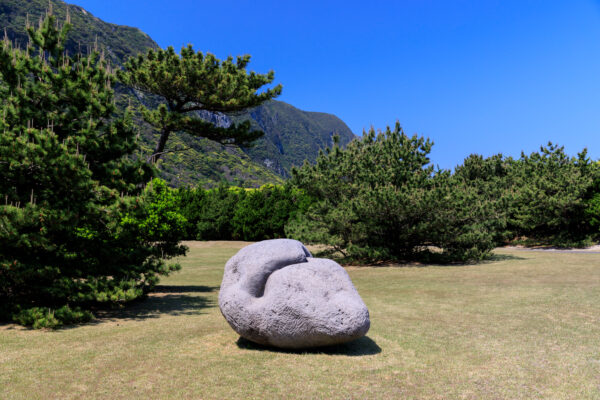 Tranquil mountain scene with lush trees, weathered boulder, and towering mountains in Habushiura Park.