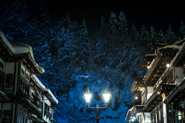 Enchanting winter night in Ginzan Onsen with snow-covered buildings under starry blue sky.