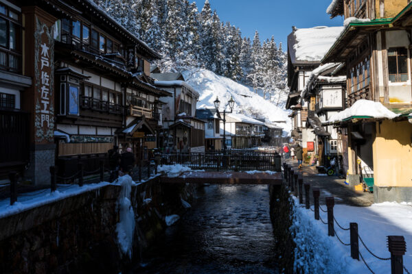 Charming winter scene in Ginzan Onsen, Japan, with traditional buildings, snow, and mountains.