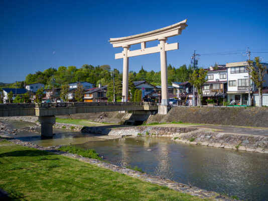 Tranquil Sakurayama Hachimangu Shrine: Majestic torii gate, lush greenery, peaceful river in Japanese setting.