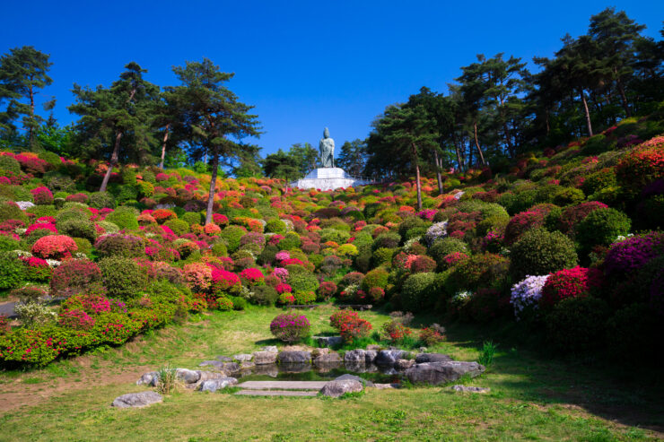 Tranquil Gardens at Shiofunekannon-ji: Lush greenery, vibrant flowers, and majestic white statue in Japan.