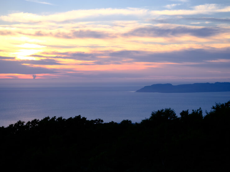 Tranquil sunset view of Rishiri Island with colorful sky, calm sea, and lush greenery.