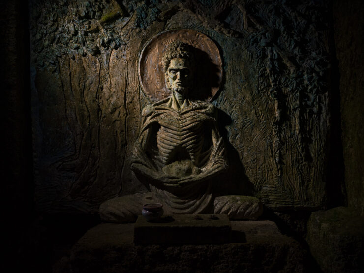 Stone-carved meditative figure in atmospheric cave setting.