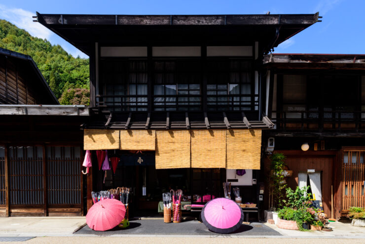 Traditional Japanese inn, lush nature, pink parasols.