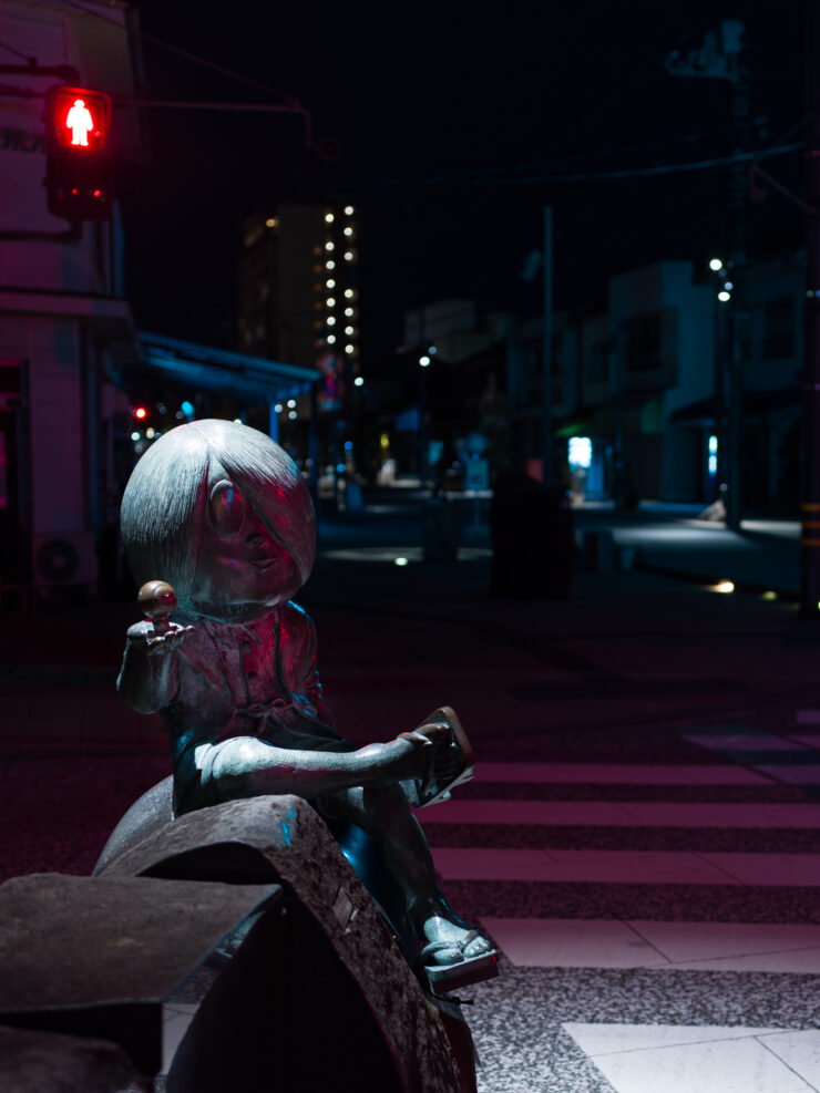 Solitary white-haired woman contemplates urban night scene.