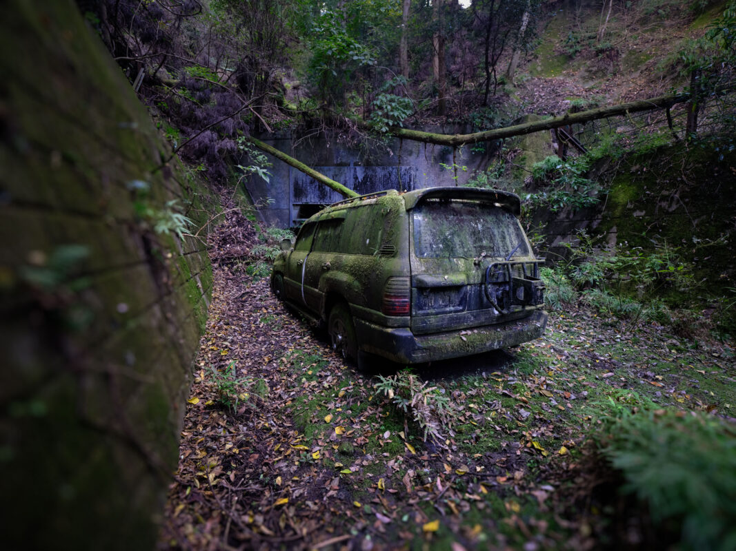 Abandoned Toyota Land Cruiser covered in moss on an overgrown forest trail