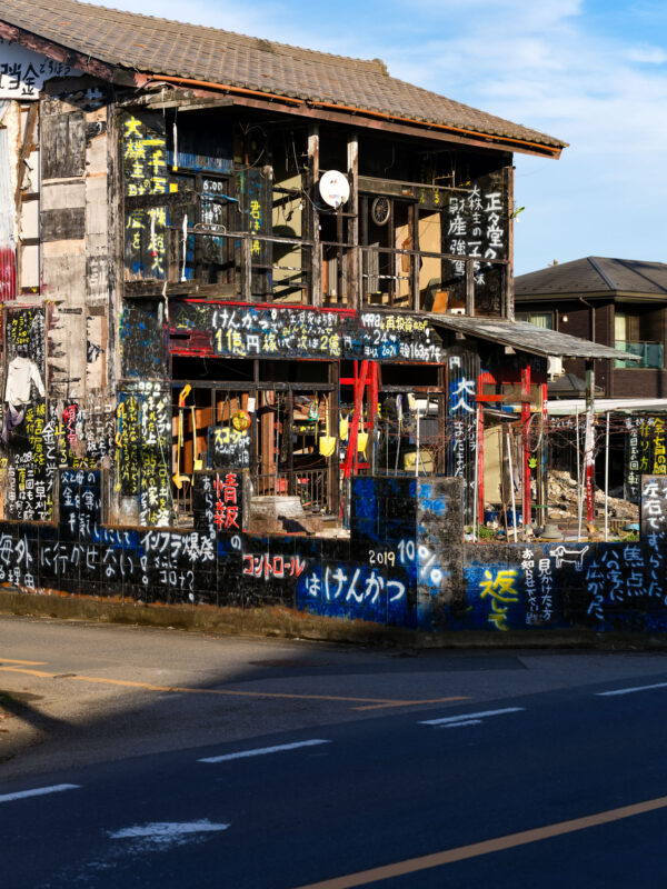 Weathered two-story black house covered in colorful graffiti text beside a clean road