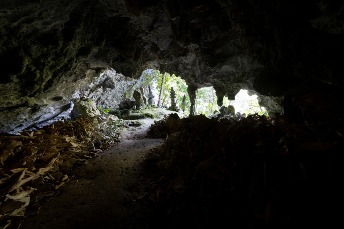 Hidden Japanese cave shrine with stone guardian statues near a sunlit entrance.
