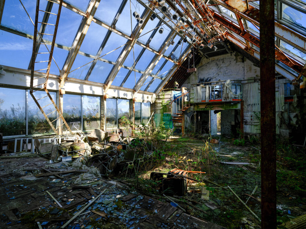 Abandoned church interior with broken glass roof, rusted beams, sunlight, and plants reclaiming debris