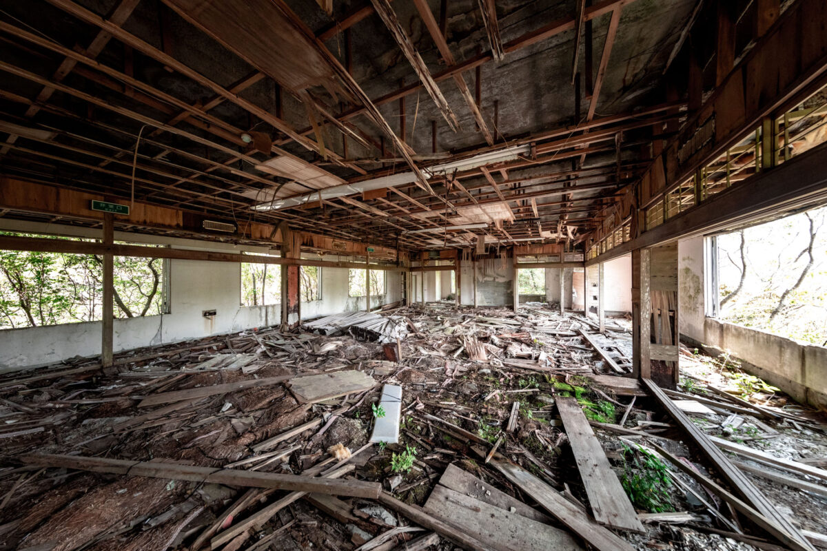 Abandoned New Muroto Sky Resort hall with exposed ceiling, debris, and window light.