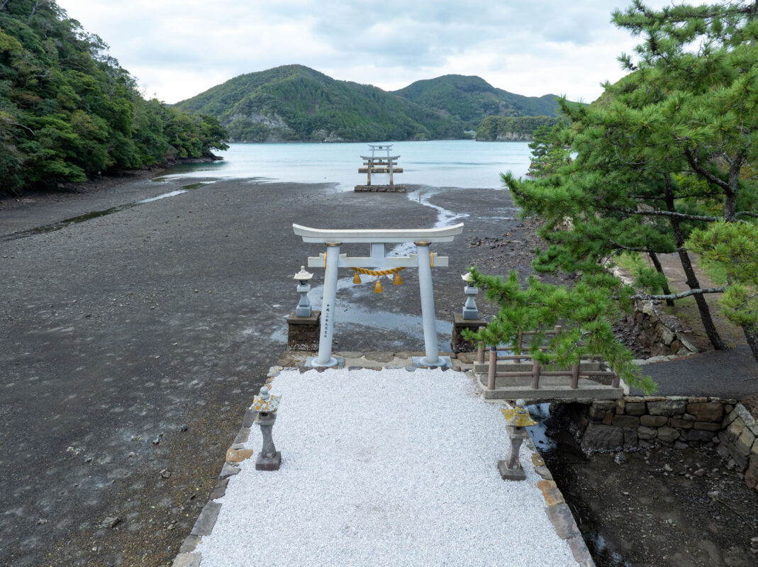 Watazumi Shrine gravel path leading to torii gates over tidal flats and sea.