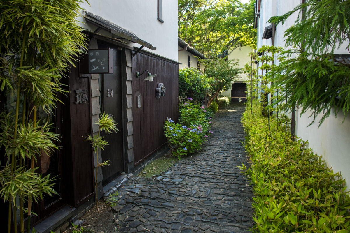 Stone-paved alley in Omihachiman, Japan, lined with traditional wooden buildings and greenery.