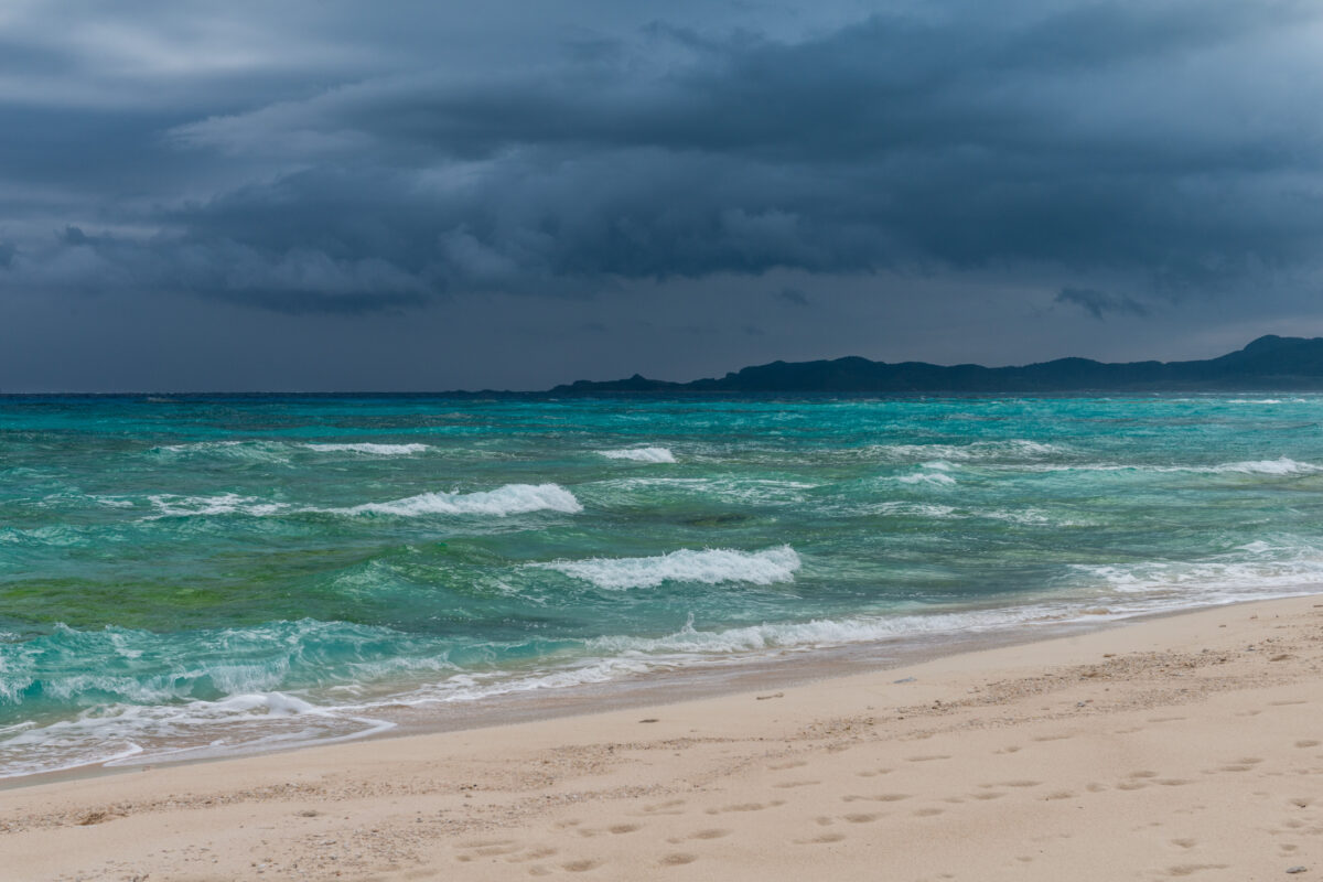 Storm clouds over turquoise ocean waves and sandy beach on Kumejima Island, Japan