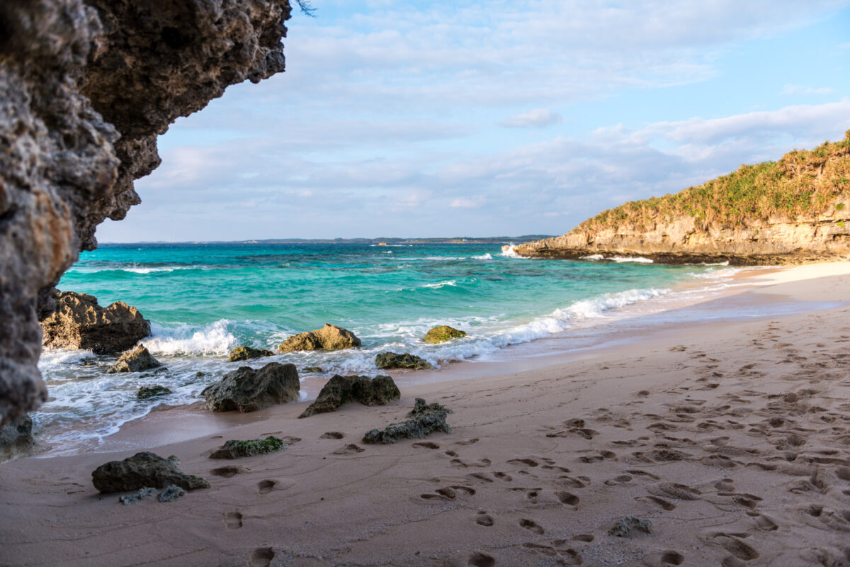 Miyako Island beach with footprints, rocky shore, and clear turquoise water under blue sky