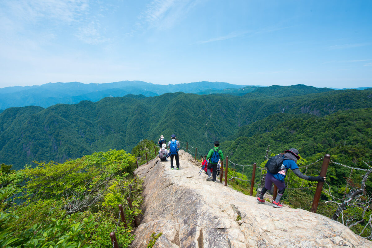 Hikers on Mount Ōdaigahara ridge trail overlooking forested mountains in Japan