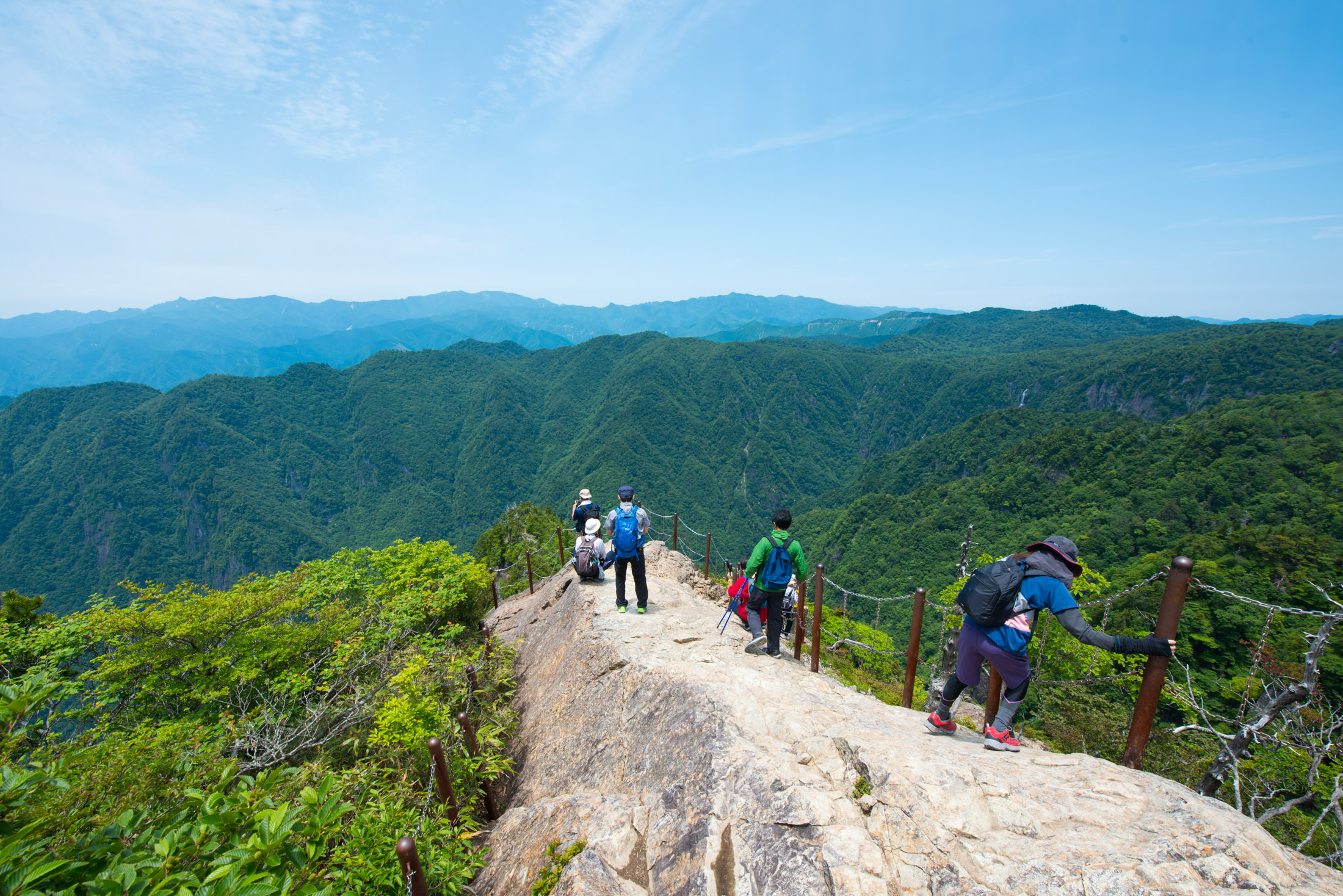 Hikers on Mount Ōdaigahara ridge trail overlooking forested mountains in Japan