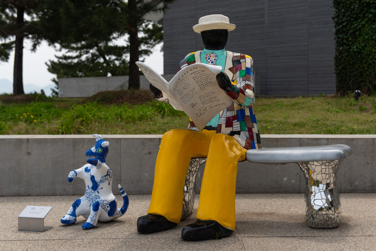 Colorful reader sculpture with blue dog on mosaic bench at Naoshima art park.