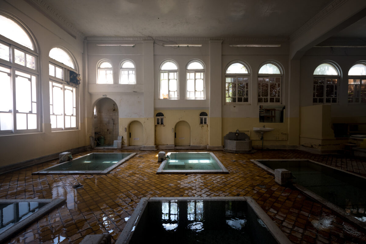 Historic Sekizenkan Ryokan onsen bath hall with arched windows and tiled hot spring pools.