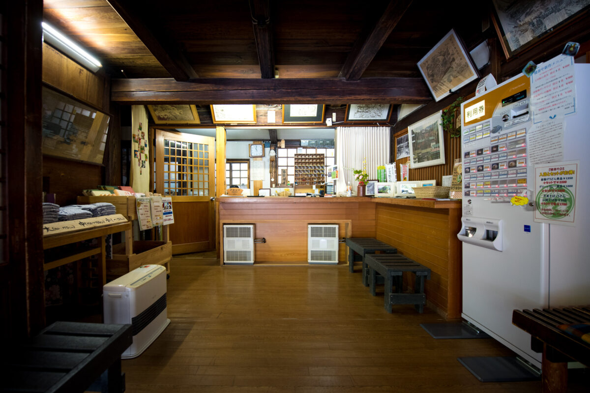 Traditional wooden reception area at Sekizenkan Ryokan, Japan, with check-in counter and vending machine.