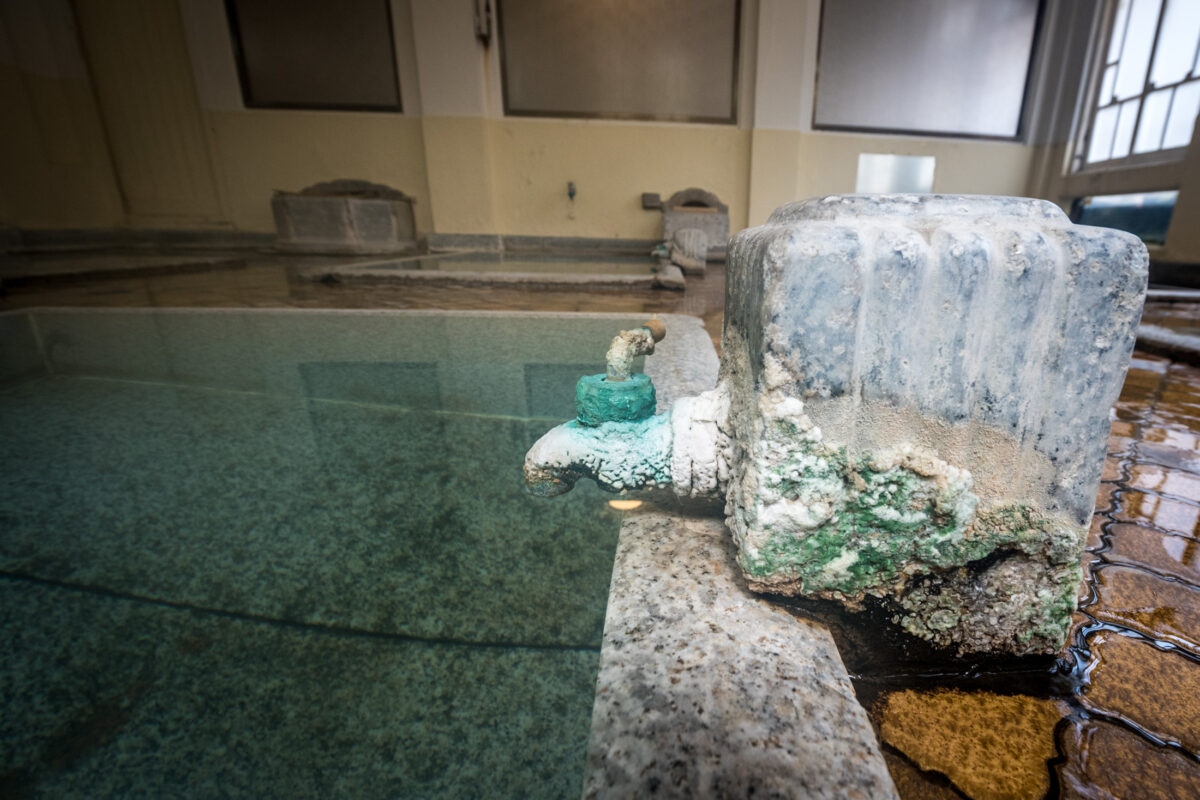 Mineral-stained stone spout pours hot spring water into Sekizenkan Ryokan indoor bath.