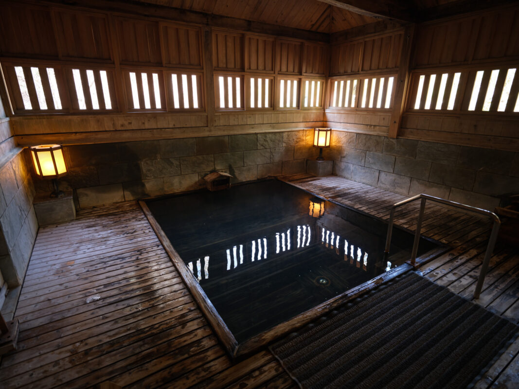 Traditional Shima Onsen indoor hot spring bath with lantern-lit wooden pool and stone walls.