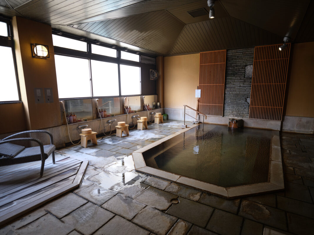 Traditional indoor stone onsen bath at Shima Onsen, Japan with steam and wooden stools.