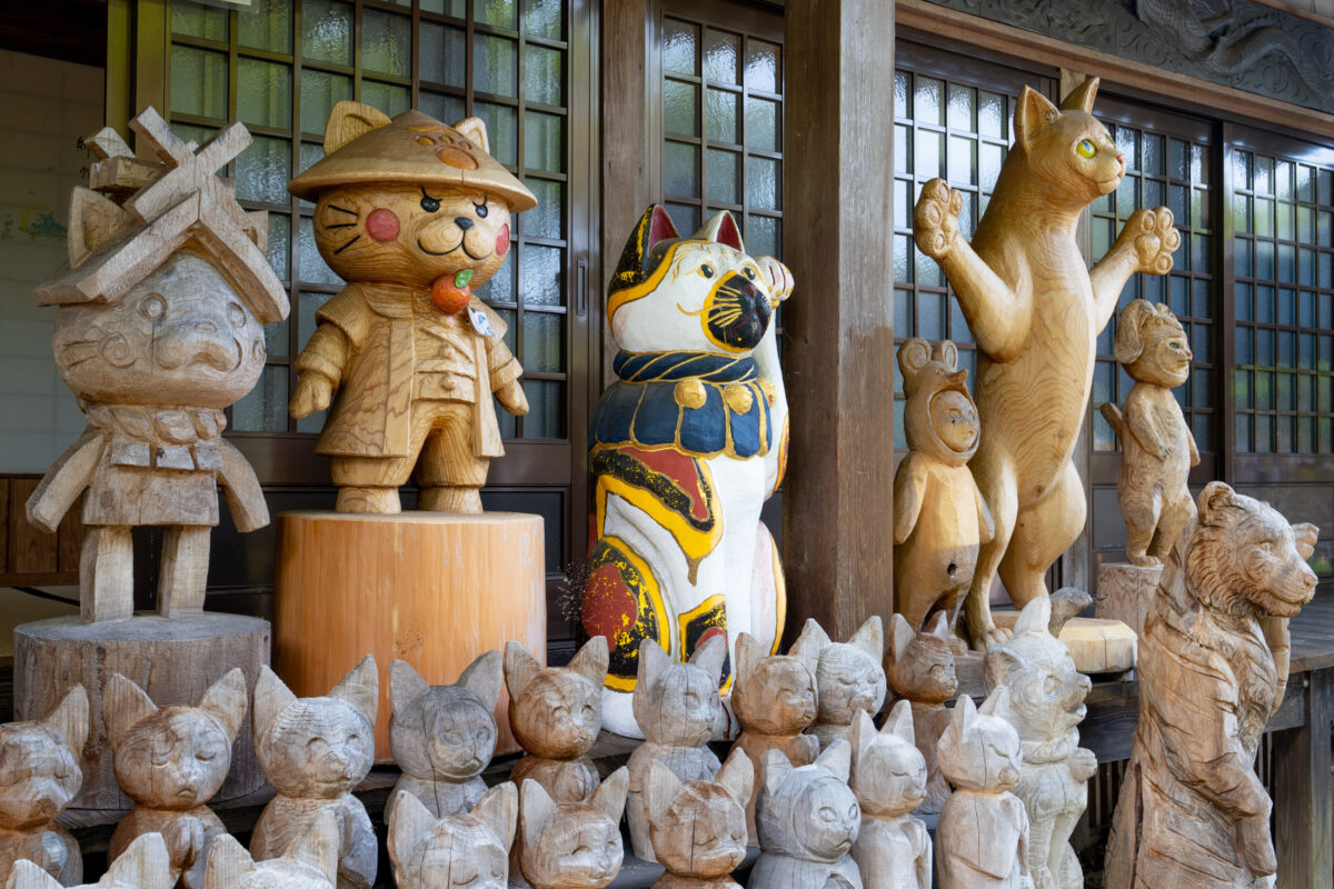 Wooden cat figurines and a painted maneki-neko display on Unrin-ji temple veranda.