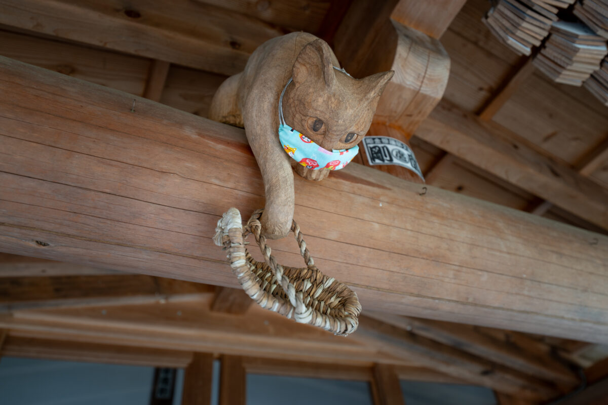 Wooden cat carving under Unrin-ji temple eaves reaching for hanging straw ring