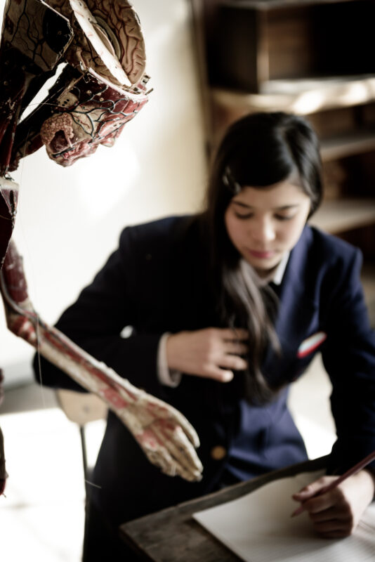 Abandoned school classroom with student studying beside realistic skeleton anatomy model