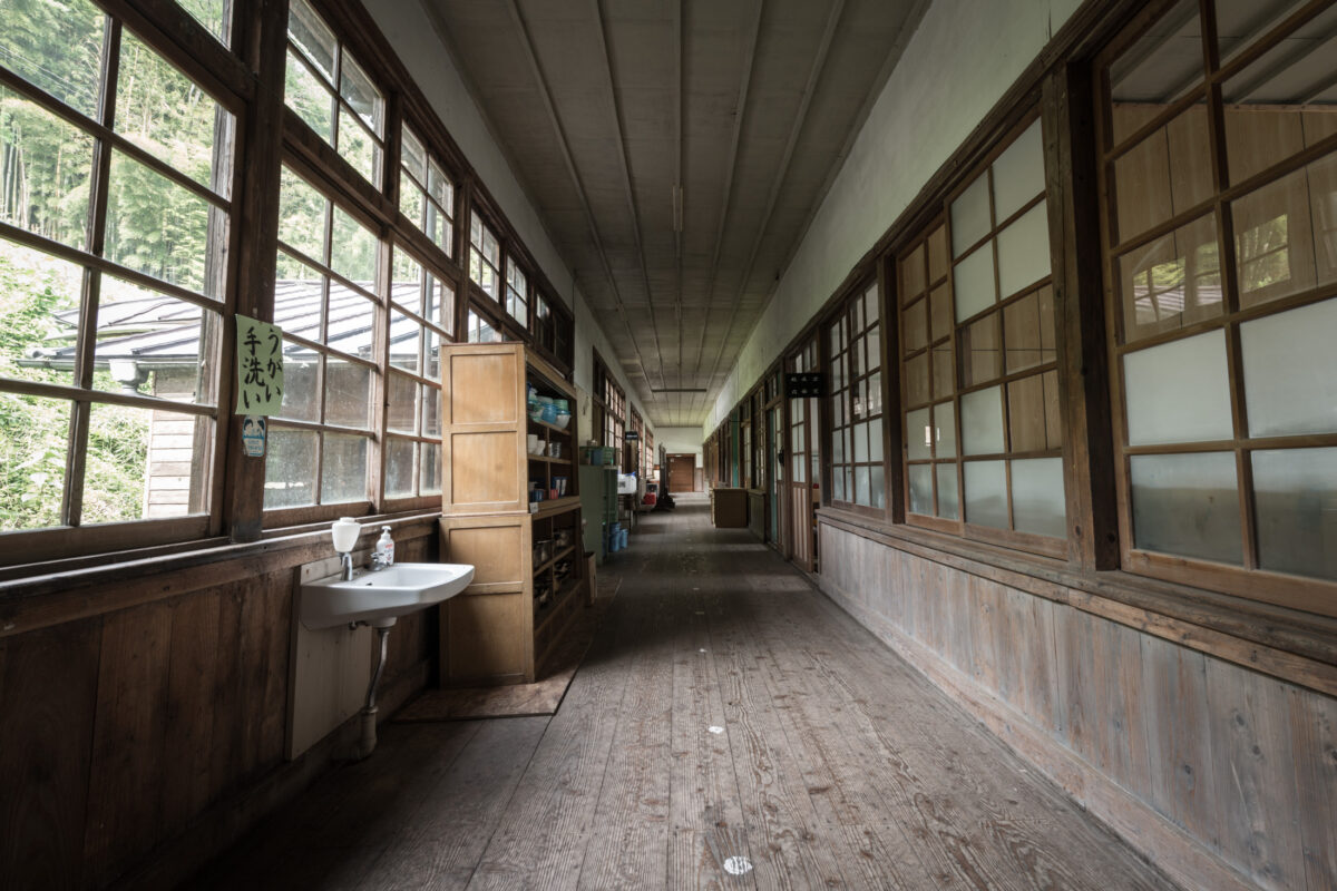 Abandoned wooden school corridor near Tokyo with sunlit windows, sink, and sliding classroom doors