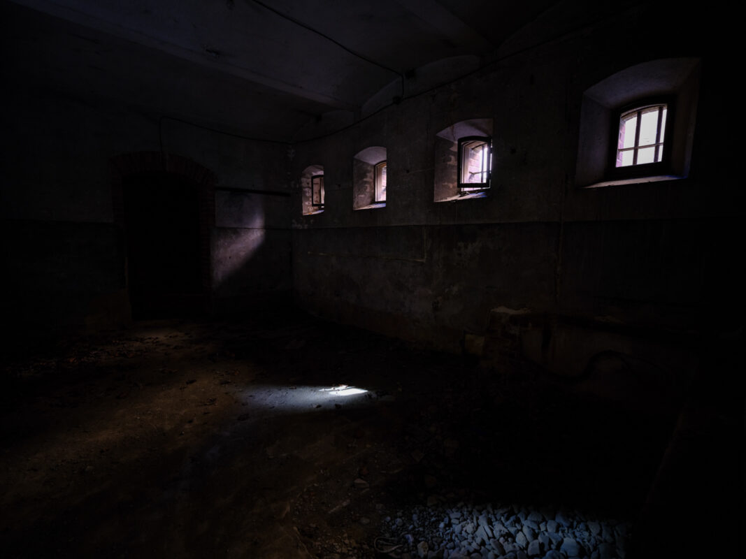 Abandoned Nara Prison corridor with barred windows and beams of light on dusty floor.