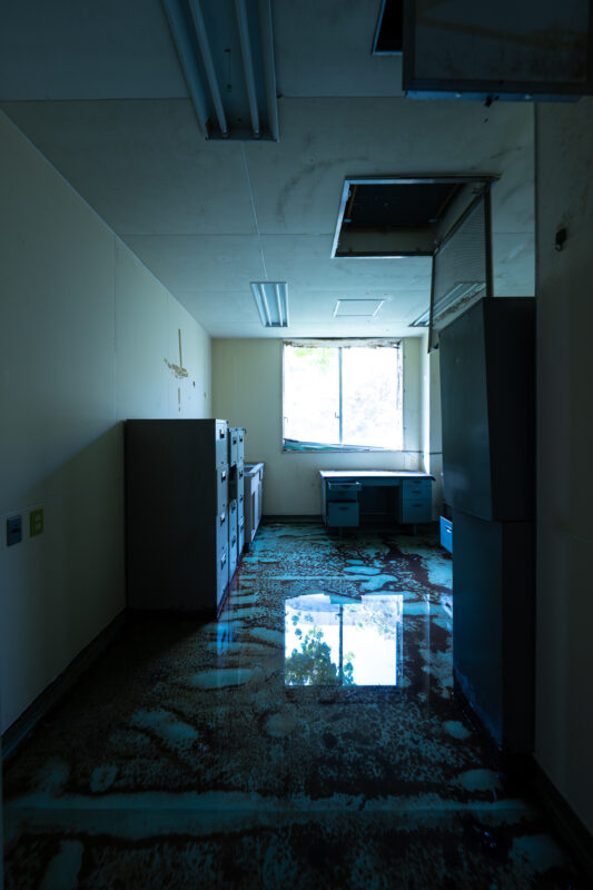Flooded corridor in abandoned animal research facility with lockers, debris, and window reflection