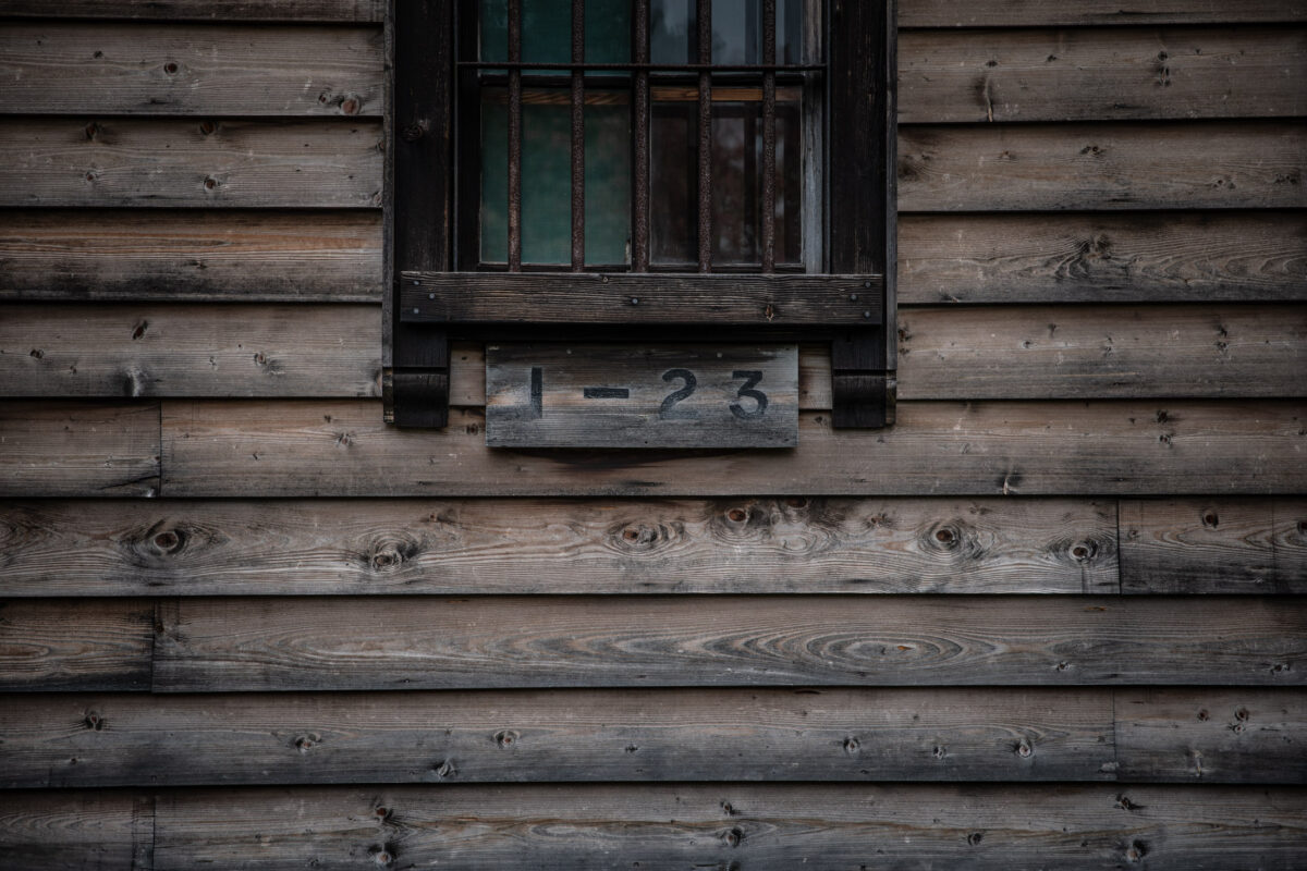 Barred window on weathered wooden wall at Abashiri Prison, Japan, marked 1-23.
