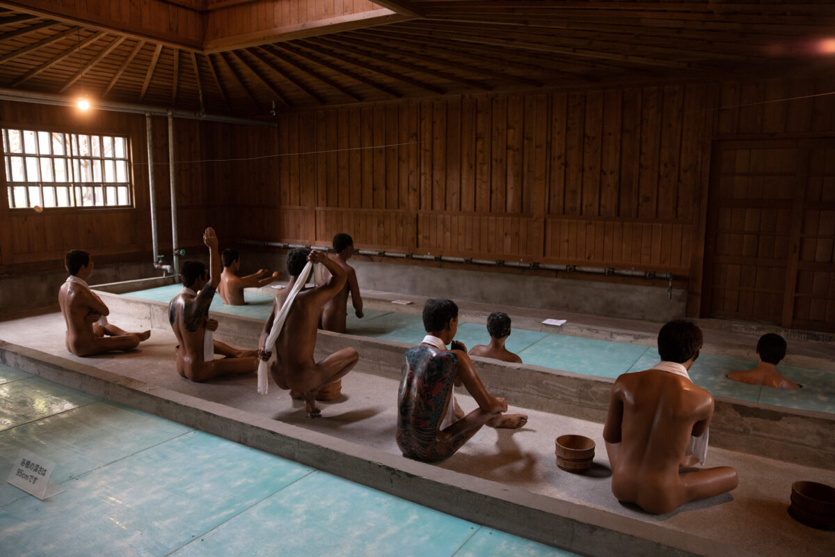 Abashiri Prison museum bathhouse reconstruction with lifelike inmate figures in wooden communal pools.