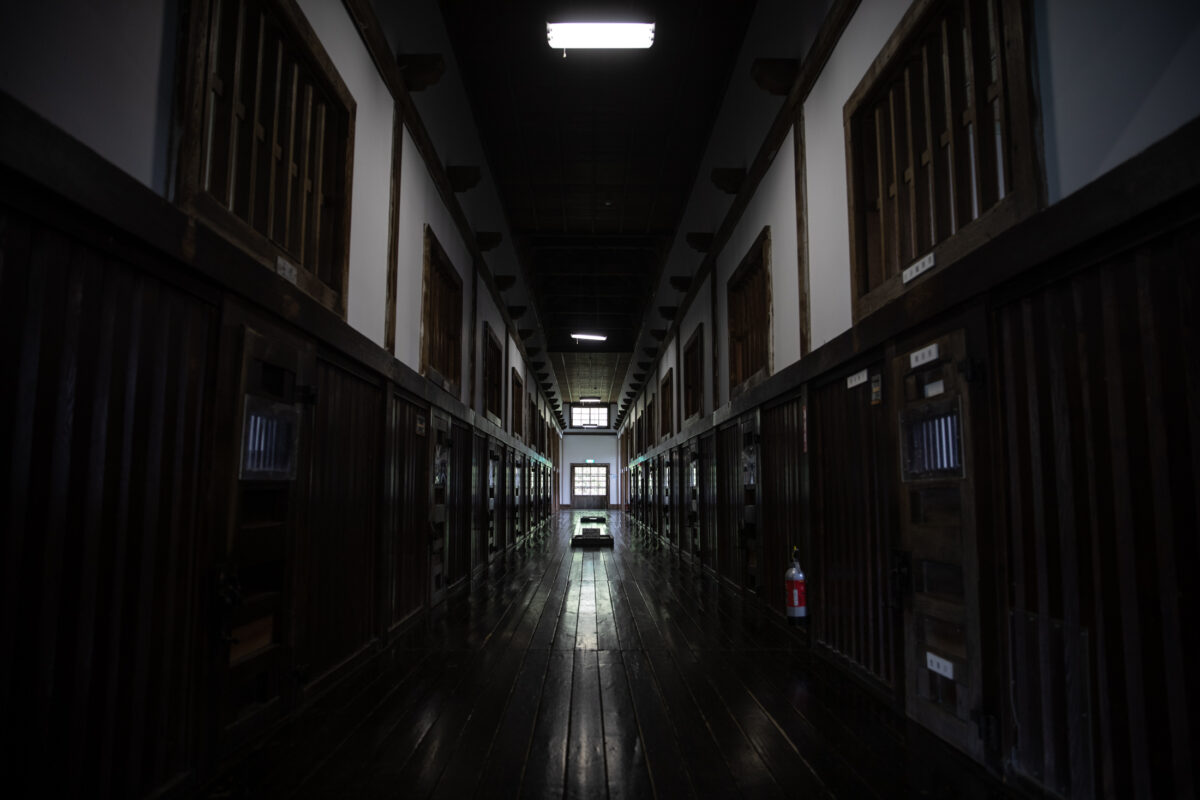 Abashiri Prison corridor with wooden floors and barred cell doors leading to a bright window.