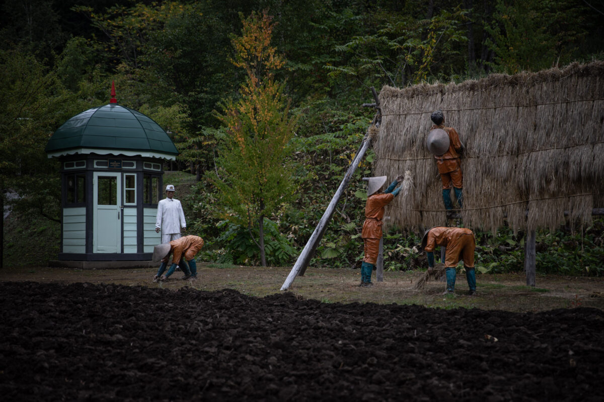 Forced labor yard at Abashiri Prison, Japan, with workers stacking straw under guard