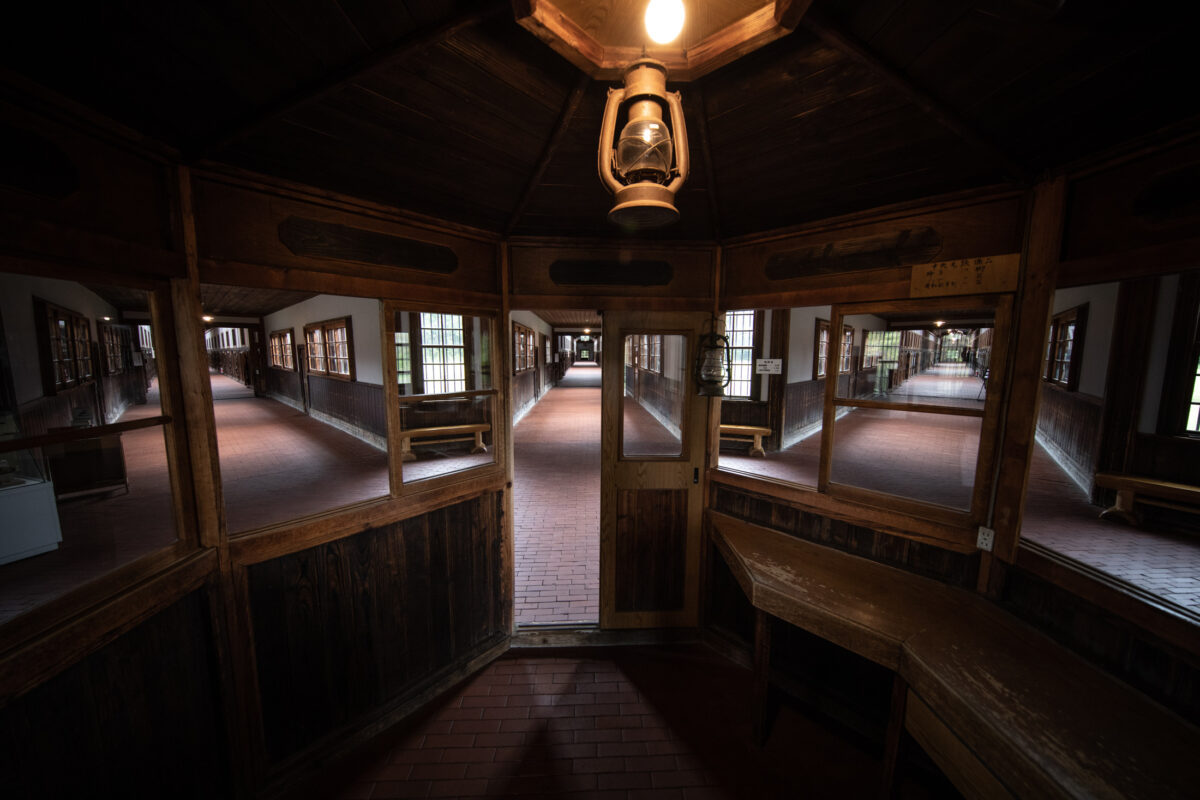 Interior view from Abashiri Prison guard booth showing symmetrical wooden corridors and hanging lantern.