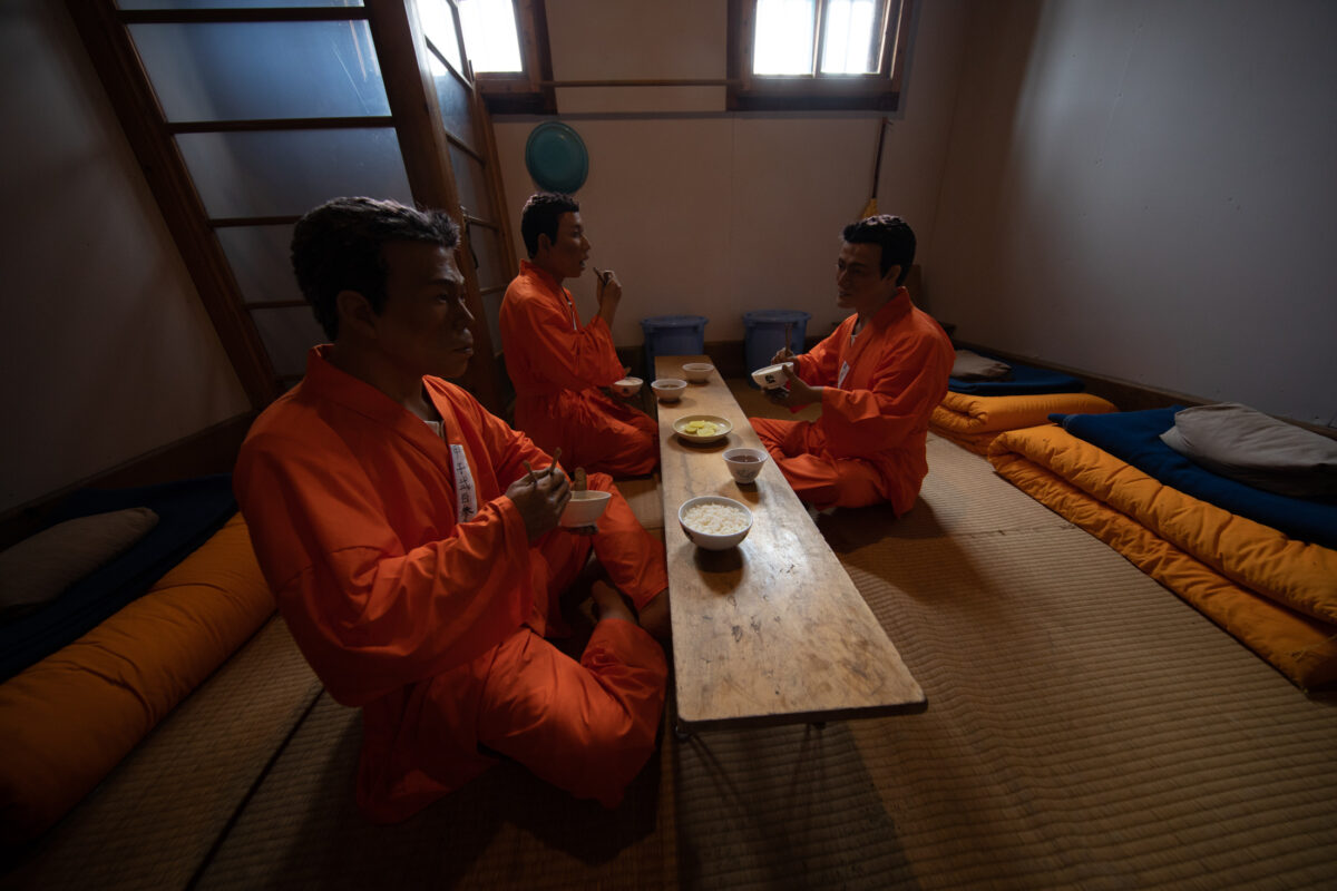 Abashiri Prison interior with inmates eating rice at a low table on tatami mats